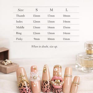May include: A sizing chart titled Find Your Perfect Fit with measurements in millimeters for thumb, index, middle, ring, and pinky fingers in sizes S, M, and L. Below, six beige press-on nails feature leopard print, pearls, gold studs, and a pink lip.