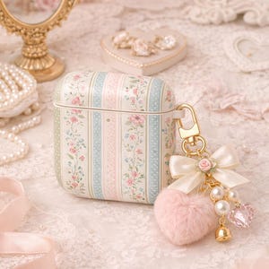 May include: Floral patterned AirPod case with a gold clasp and a pink heart-shaped charm. The case features a design of pink and blue stripes with floral accents. A white bow and pearl accents complete the charm.