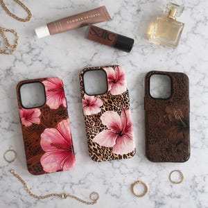 May include: Three phone cases with floral and animal print designs. One case features pink hibiscus flowers on a brown background, another has pink flowers on a leopard print, and the third has a brown embossed floral pattern. Accessories include jewelry and cosmetics.