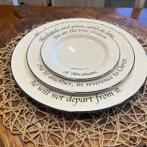 May include: Two stacked off-white ceramic plates with black rims and black printed text. The top plate reads: Husbands and wives yield in love, You are the true children, Galatians 3:29, of Abraham. The bottom plate reads: one to another, in reverence to Christ. he will not depart from it.