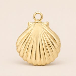 May include: A gold-toned metal charm shaped like a scallop shell. The charm features a fan-like design with raised vertical ridges radiating from the base toward the rounded edge. A small, circular jump ring is attached to the top for hanging.