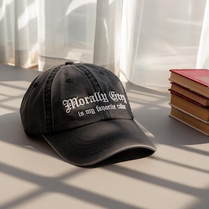 Puede incluir: Gorra de béisbol negra con el texto blanco "Morally Grey is my favorite color". La gorra está hecha de un material suave y tiene una visera curva. Se encuentra sobre una superficie gris claro.