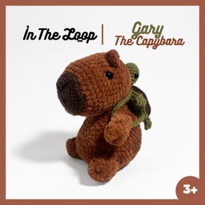 May include: A handmade brown crocheted capybara plush toy with a smaller green crocheted turtle on its back. The text "In The Loop | Gary The Capybara" is above the toy. The toy is suitable for ages 3 and up.