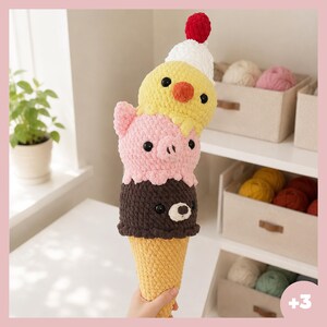 Peut inclure: Un jouet en peluche au crochet en forme de cornet de glace à trois boules. La boule inférieure est marron foncé avec un visage d'ours, celle du milieu est rose clair avec un visage de cochon, et celle du haut est jaune avec un visage de poussin.