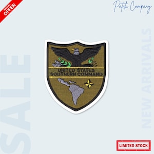 May include: A shield-shaped patch with a black eagle, olive branches, and the text "UNITED STATES SOUTHERN COMMAND." The patch features a map of South America and a yellow star. The patch is on a white background with the words "SALE" and "NEW ARRIVALS."