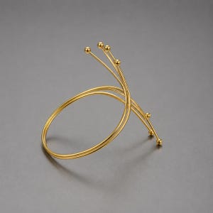 Puede incluir: Un brazalete de metal en tono dorado con una banda circular que se eleva en espiral hacia cuatro tallos de alambre finos y radiantes. Cada tallo termina en una pequeña cuenta esférica pulida, creando un diseño abierto y estructurado.