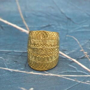 May include: A gold-colored ring with intricate geometric patterns. The ring features a series of bands with repeating designs, including diamond, spiral, and linear motifs. The ring's surface has a textured appearance, and the overall design suggests a historical or cultural significance.