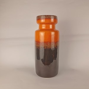 Può includere: Un vaso cilindrico alto in ceramica con finitura lucida e una netta transizione di colore. La sezione superiore è di un arancione vivace, mentre la parte inferiore è di un marrone scuro, con una sfumatura maculata e testurizzata tra i colori.