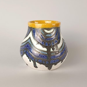 Può includere: Un vaso in ceramica dal corpo largo e arrotondato con finitura smaltata a craquelé. Il design presenta un bordo giallo senape, con bande alternate di bianco, azzurro e blu scuro, sovrapposte a motivi verticali color marrone scuro a goccia.