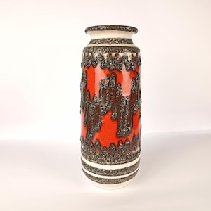 Può includere: Un vaso cilindrico in ceramica caratterizzato da una vivace smaltatura arancione contrastata da motivi a goccia testurizzati color marrone scuro simili alla lava. Il design include fasce orizzontali marroni sulla parte superiore e inferiore.