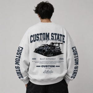 May include: A light grey crewneck sweatshirt featuring dark blue text and a graphic of a modified sports car on the back. The text reads CUSTOM STATE, UNDERGROUND, BUILT DIFFERENT, and includes additional small print and the year 2024.