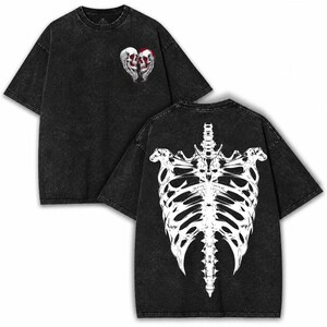 Puede incluir: Una camiseta negra con efecto lavado ácido que presenta un pequeño gráfico en el pecho de dos calaveras formando un corazón. La parte posterior de la camiseta muestra un gráfico blanco grande y detallado de una caja torácica y columna.