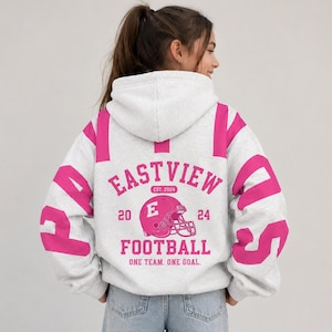 May include: A light grey hooded sweatshirt featuring bright pink accents on the sleeves and back. The back graphic displays a pink football helmet, the text EASTVIEW FOOTBALL, EST. 2024, and the phrase ONE TEAM. ONE GOAL. with the numbers 20 and 24.