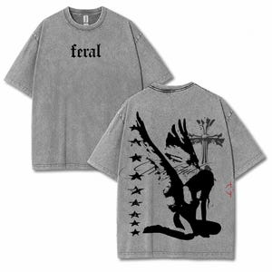 May include: Gray t-shirt with the word "feral" printed on the front. The back of the shirt features a black graphic of an angel with a cross and stars. The shirt has a vintage, washed look.