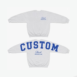 Peut inclure: Un sweat-shirt à col rond gris clair avec un petit logo bleu en écriture cursive sur le devant indiquant Rush SOCCER CLUB. Le dos du sweat-shirt affiche le mot CUSTOM en grandes lettres bleues au-dessus du logo Rush SOCCER CLUB.