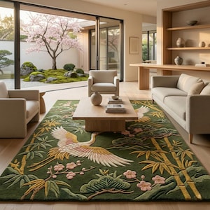 May include: A green rug with a Japanese crane design. The rug features a large crane with white and gold wings, bamboo stalks, and pink cherry blossoms. The rug is placed in a modern living room with neutral-toned furniture.
