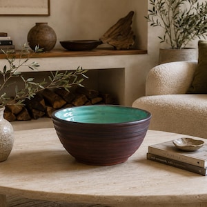 May include: A large, round ceramic bowl with a dark brown, textured exterior and a smooth, vibrant turquoise interior. The bowl features subtle horizontal ridges along its outer surface, creating a tactile, hand-thrown appearance for this vessel.