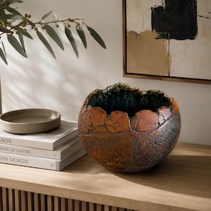 May include: A round, bowl-shaped ceramic vessel with a highly textured, cracked exterior in shades of burnt orange and dark brown. The interior of the bowl features a deep, dark blue glaze, and the rim has an irregular, jagged, and organic edge.