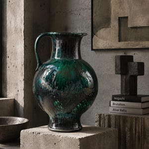 May include: A large, round ceramic pitcher with a glossy, dark emerald green and black drip glaze finish. The vessel features a wide, flared rim, a curved handle on one side, and a narrow base, showcasing a textured, multi-tonal surface.