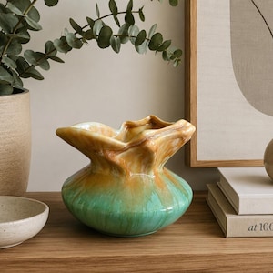May include: A ceramic vase with a wide, ruffled opening and a rounded base. The glaze features a gradient transition from a warm, marbled amber and tan colour at the top rim to a vibrant, solid turquoise green finish on the lower body section.