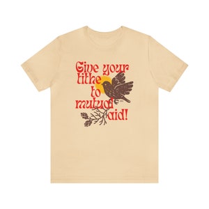 May include: A beige t-shirt with a red graphic that says "Give your tithe to mutual aid!" with a brown bird and a branch with green leaves.