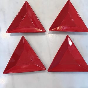 May include: Four bright red, triangular-shaped serving dishes. Each dish has a glossy finish and a slightly raised edge. The dishes are arranged in a square formation, perfect for serving appetizers or small portions.