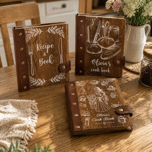 May include: Three rectangular recipe books with dark brown leather-like spines featuring gold-tone metal rivets. The covers are wood-textured with white line art illustrations and text including Recipe & Book, Olivia's cook book, and Olivia's Cook Book.