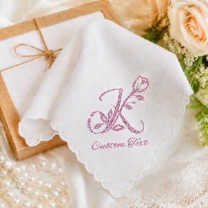 Könnte beinhalten: Ein weißes Stofftaschentuch mit gewelltem Rand, verziert mit einem pinkfarbenen, glitzernden Buchstaben K, der mit Rosenmotiven gestaltet ist, sowie dem Text Custom Text in einer passenden pinkfarbenen Glitzerschrift auf dem Stoff.