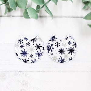 May include: Two white round ornaments with a snowflake pattern in shades of blue and silver. The ornaments have a cut-out section at the top.