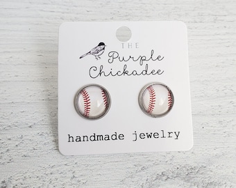 Peut inclure: Une paire de boucles d'oreilles à clous argentées avec un motif de balle de baseball. Les boucles d'oreilles sont sur une carte blanche avec le texte "The Purple Chickadee handmade jewelry".