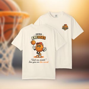 Puede incluir: Dos camisetas color crema. Una camiseta presenta un personaje de dibujos animados de baloncesto haciendo malabarismos con una pelota, con el texto "ZERO EXCUSES" y "Call me clutch. See you on the court." La otra camiseta tiene un pequeño logo que dice "NO EXCUSES".