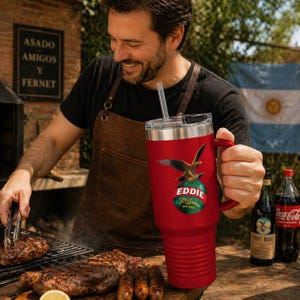 May include: A red insulated tumbler with a handle and a straw. The tumbler features a logo with an eagle and the text "Eddie Joe Branca Milano". The image shows a grilling scene with food and drinks.