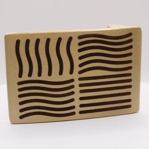 Peut inclure: Un bloc de bois clair avec des dessins au trait marron foncé. Le bloc est rectangulaire avec quatre sections distinctes de dessins au trait, comprenant des lignes ondulées et droites. Le design rappelle les symboles élémentaires.