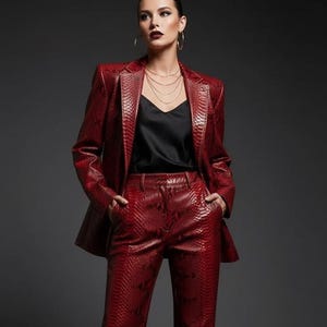 May include: A red snakeskin-patterned suit, consisting of a blazer and matching pants, paired with a black top. The suit has a textured appearance and a tailored fit. The model is wearing black shoes and gold jewelry.