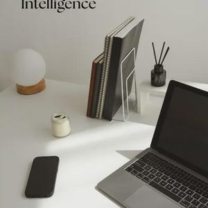 May include: A workspace featuring a laptop, smartphone, and notebooks. The text "AI guide Your Guide to Artificial Intelligence" is displayed. A small candle, a lamp, and a diffuser are also present on the white surface.