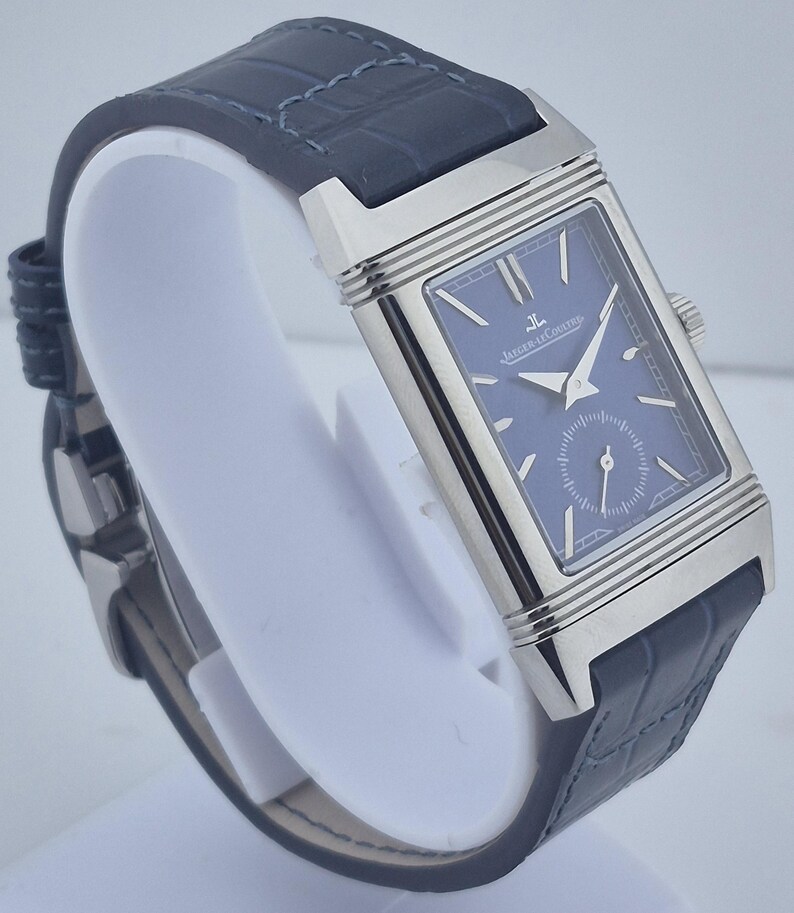 Pu&ograve; includere: Un orologio da polso rettangolare con quadrante blu e cassa color argento. L'orologio ha un cinturino in pelle blu scuro. Il quadrante dell'orologio presenta il marchio "Jaeger-LeCoultre".