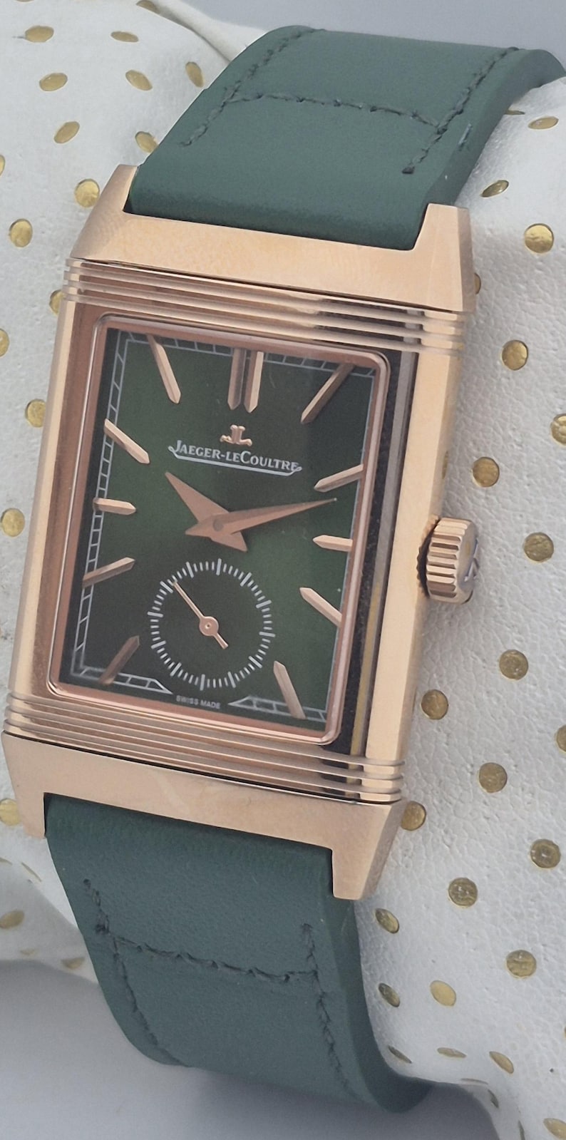 May include: A luxury wristwatch with a rectangular rose gold case and a green leather strap. The watch face is green with rose gold hands and markers, and features the Jaeger-LeCoultre logo. The watch has a small seconds dial and the words "SWISS MADE".