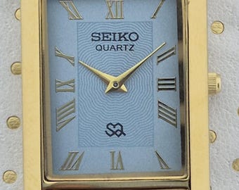 Reloj Seiko de cuarzo vintage: esfera azul claro, correa marrón.