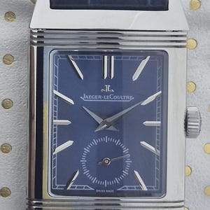 Pu&ograve; includere: Un orologio da polso rettangolare in acciaio inossidabile con quadrante blu navy e cinturino in pelle abbinato. Il quadrante dell'orologio presenta lancette e indici argentati, un piccolo quadrante dei secondi e il logo Jaeger-LeCoultre.