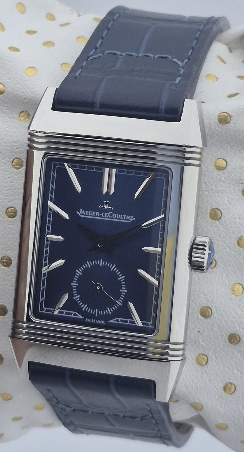 Pu&ograve; includere: Un orologio Jaeger-LeCoultre rettangolare in acciaio inossidabile con quadrante blu navy e cinturino in pelle abbinato. L'orologio presenta lancette e indici argentati, un piccolo quadrante dei secondi e la scritta "SWISS MADE".