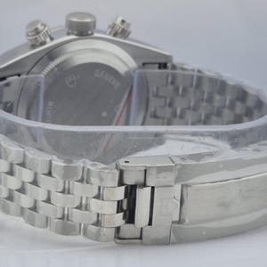 May include: A silver-toned wristwatch with a stainless steel band. The watch face is not visible, but the back of the watch is visible, with the word "Geneve" and other text. The watch is new and still has protective plastic.