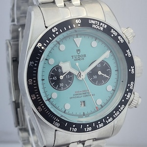 May include: A stainless steel Tudor Geneve chronograph watch with a light blue dial, black bezel, and a stainless steel bracelet. The watch features subdials, a date window, and is officially chronometer certified.