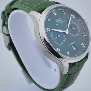 May include: A luxury wristwatch with a green dial and a green leather band. The watch has a silver-colored case and features the text "IWC SCHAFFHAUSEN" on the dial. The watch also has two sub-dials and a date display.