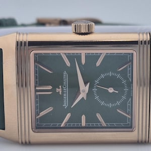 May include: A rectangular gold-toned wristwatch with a green face and a small seconds dial. The watch features gold hands and markers, and a green leather strap. The watch is a Jaeger-LeCoultre.
