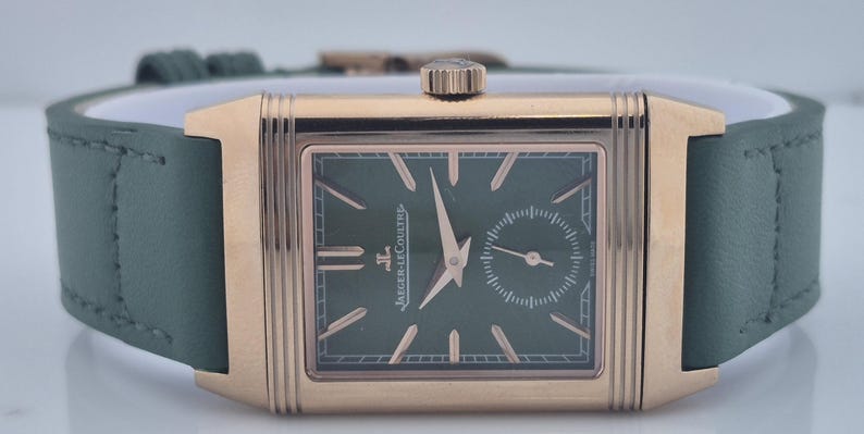 May include: A rectangular gold-toned wristwatch with a green face and a small seconds dial. The watch features gold hands and markers, and a green leather strap. The watch is a Jaeger-LeCoultre.