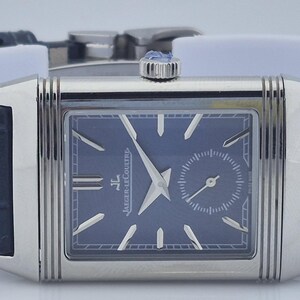Pu&ograve; includere: Un orologio da polso rettangolare argentato con quadrante blu scuro e un piccolo quadrante dei secondi. L'orologio ha lancette e indici argentati e un cinturino in pelle blu scuro. L'orologio &egrave; esposto su un supporto bianco.