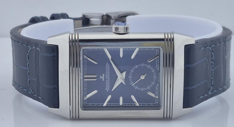 Pu&ograve; includere: Un orologio da polso rettangolare argentato con quadrante blu scuro e un piccolo quadrante dei secondi. L'orologio ha lancette e indici argentati e un cinturino in pelle blu scuro. L'orologio &egrave; esposto su un supporto bianco.