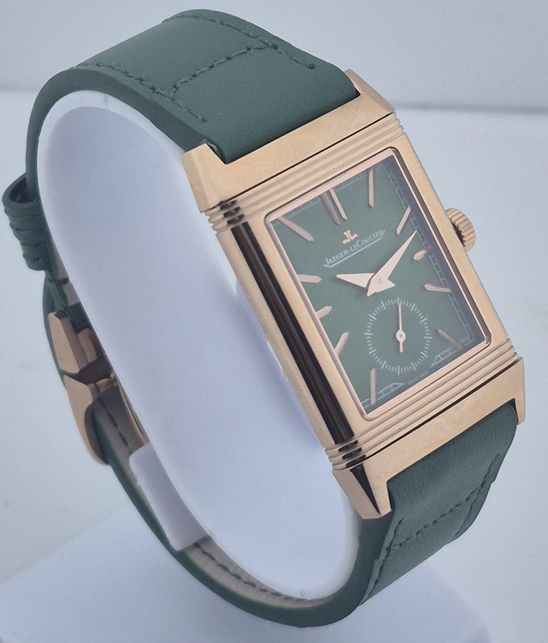 May include: A rectangular wristwatch with a green face and a green leather band. The watch has a gold-colored case and a small seconds dial. The watch is displayed on a white stand.