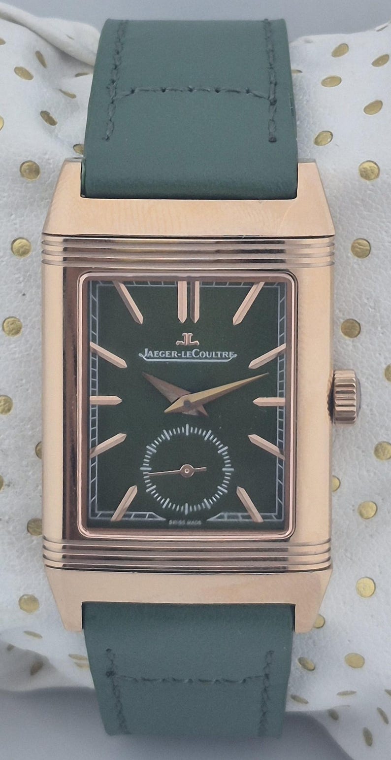 May include: A rectangular rose gold wristwatch with a dark green face and a small seconds dial. The watch features gold hands and markers, and a green leather strap. The watch face has the text "JAEGER-LECOULTRE" and "SWISS MADE".