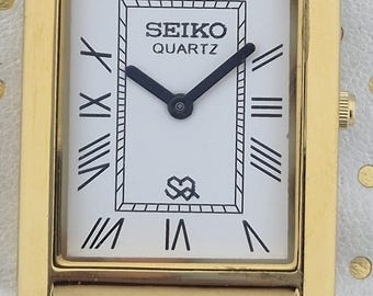 Reloj Seiko de cuarzo vintage: esfera blanca, correa negra.